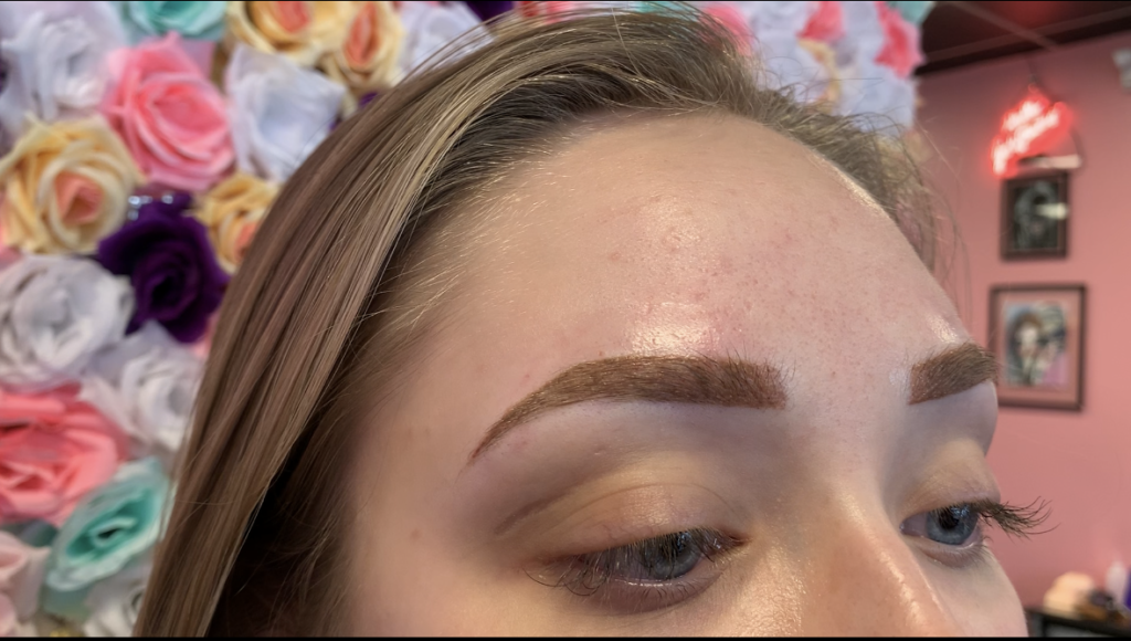 Close-up of freshly microbladed or ombre brows at Just Browzin' lash and brow studio in Toledo, Ohio, showcasing perfectly shaped and defined arches against a floral background.