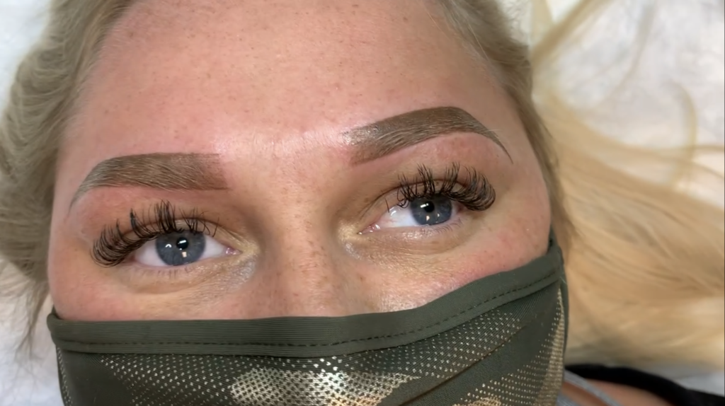 Close-up of a client's face at Just Browzin' studio in Toledo, Ohio, showcasing freshly completed ombre brows and beautiful volume eyelash extensions, with the client wearing a camouflage face mask.